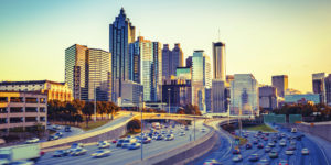 Image of downtown Atlanta taken over lanes of traffic on Interstate 75. Cars on on the road and the sun is reflecting off the buildings