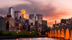 A picture taken of Minneapolis at sunset. The sky is a mixture of pink and purple hues reflected off the water