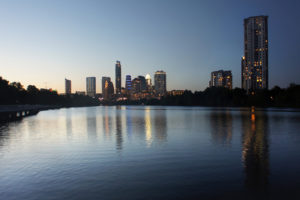 Photo of Austin, Texas downtown skyline in mid afternoon with buildings reflecting off the water.